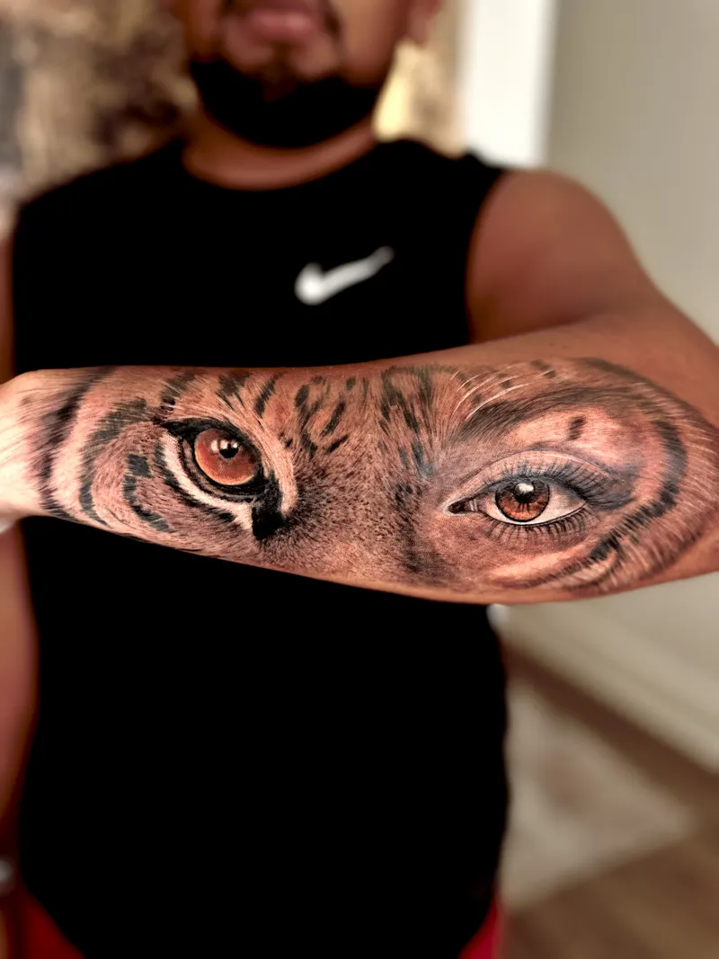 Realistic tiger eyes tattoo in colour across both forearms