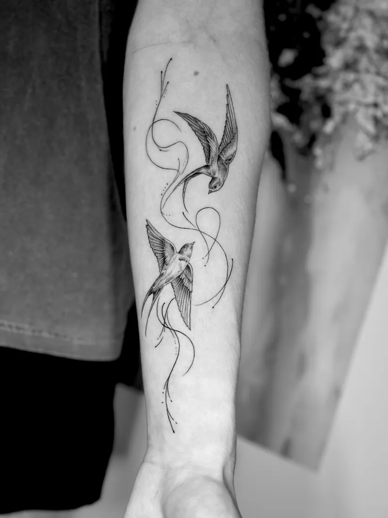 Fine line swallows with a flowing ribbon on the forearm